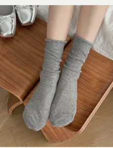 Detalle de calcetines slouch grises con borde enrollado, presentados sobre taburete de madera.