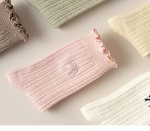 Close-up detail of cute ribbed socks with ruffled lace edge and embroidered bow design.