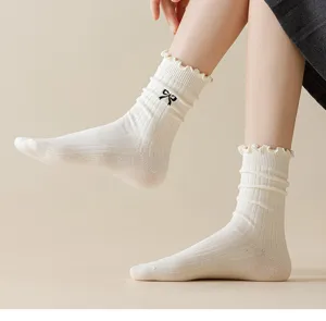 Close-up detail of white ribbed mid-calf socks featuring a cute black bow and ruffled lace cuff.