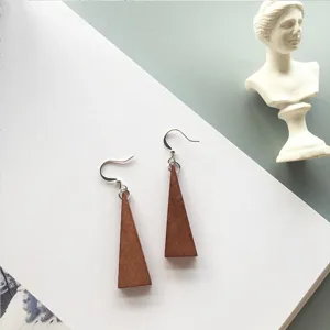 Macro view of minimalist brown wooden triangle drop earrings on a white surface