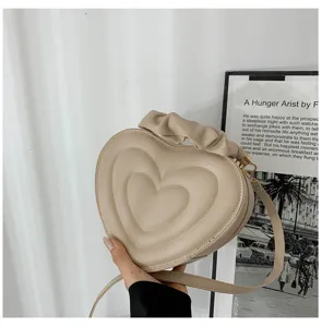 Close-up of beige heart-shaped crossbody bag with ruffled handle detail.