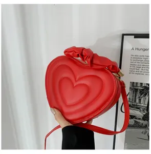 Close-up of a stylish red heart-shaped crossbody bag with ruffled handle detail