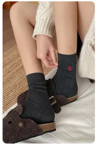 Gros plan détaillé de chaussettes mi-mollet en tricot côtelé gris foncé avec broderie d'abeille rouge.