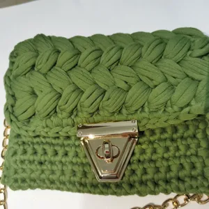 Detail shot of green handmade crochet mobile phone bag with gold metal clasp and chain strap.