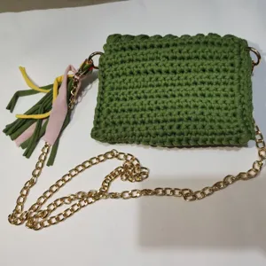 Green crochet phone bag detail, handmade fabric pouch with gold chain and colorful tassels.
