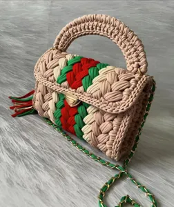 Handmade crochet fabric shoulder bag detail featuring red green weave and golden metal clasp.