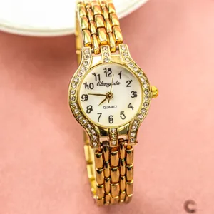 Détail de montre quartz femme, bracelet chaîne métal doré, lunette strass, chiffres clairs.