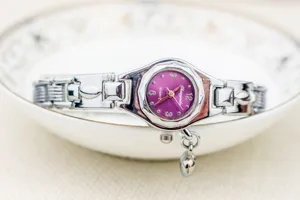 Vista detallada del bonito reloj de cuarzo para mujer con esfera morada y colgante.