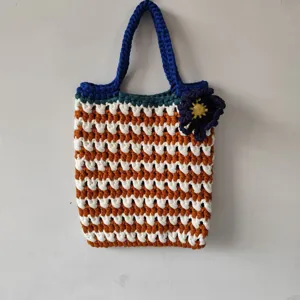 Handgemaakte gehaakte shopper detail met gestreept patroon en blauwe bloemaccent.