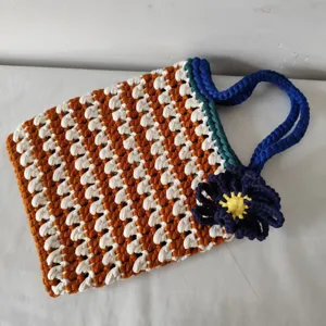 Handgemaakte gehaakte shopper tas met bruin wit patroon blauwe handgreep en bloemdecoratie.