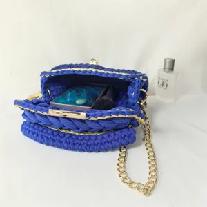Detail shot of handmade blue crochet handbag with gold chain strap and metallic woven trim.