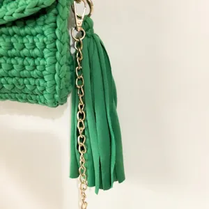 Green crochet bag detail showing textured fabric, gold chain strap, and decorative tassel.