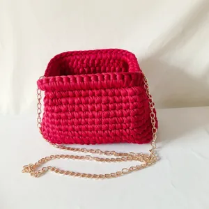 Handmade crochet shoulder bag detail, dark pink fabric crossbody clutch with gold chain strap.
