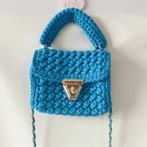 Handmade blue crochet handbag detail, knitted fabric shoulder bag with metal chain and lock.