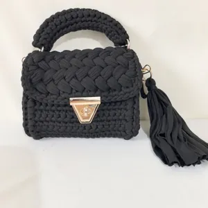Close-up view of a black handmade crochet handbag with chunky braided handle and gold metal clasp.