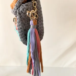 Handmade crochet fabric bag detail featuring grey knit texture and colorful fringe tassel.