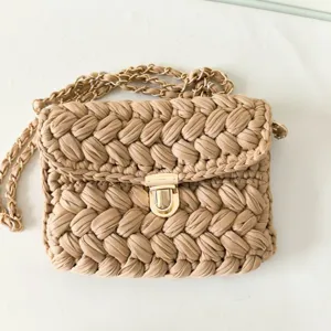 Handcrafted crochet crossbody bag detail showing beige woven fabric and metallic chain strap.