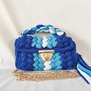 Detailed shot of handmade blue and white crochet handbag with gold chain strap and metal lock.