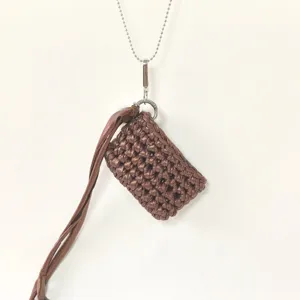 Closeup of the brown handmade woven mini earphone bag with metal chain and tassel detail.