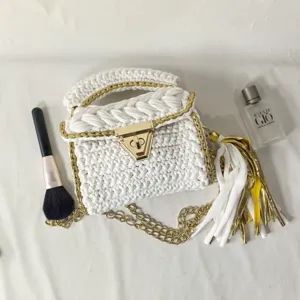 Detail view of handmade white crochet handbag with metallic gold chain and twist lock clasp.