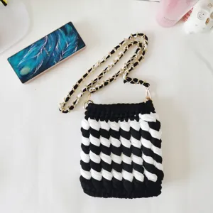 Detail view of black and white crocheted crossbody bag with metallic chain strap.