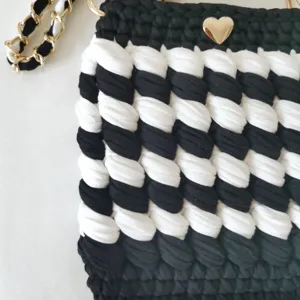 Detailed view of handmade black and white crochet crossbody bag texture with gold chain strap.