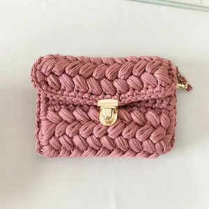 Detail view of pink handmade crochet crossbody bag, soft fabric yarn surface and metallic clasp.