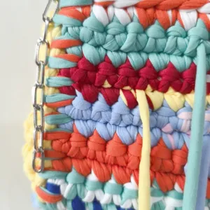 Close-up detail of colorful handmade t-shirt yarn crochet fabric with metal chain strap.