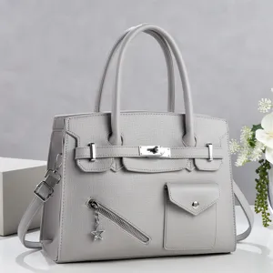 Détail de sac à main gris avec serrure métallique, poignées robustes et poche avant.