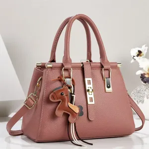 Primer plano de elegante bolso de mano de cuero rosa con herrajes dorados y dije de caballo.