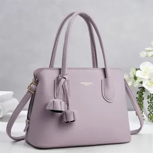 Detail view of the lavender litchi leather handbag featuring delicate double handles and tassels.