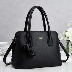 Detailed view of black pebble leather handbag with dual top handles and stylish tassel charm.