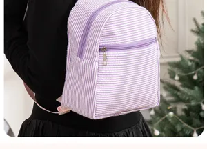 Purple and white striped seersucker backpack detail view, casual style with front zip pocket.