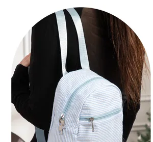 Close-up view of the blue and white striped seersucker backpack showing the front zipper pocket.