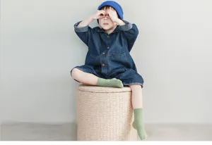 Detail shot of kids ribbed combed cotton green socks worn by a model sitting on a stool.