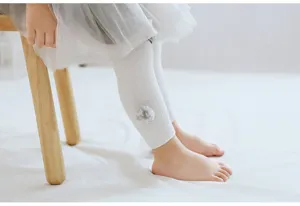 Vue détaillée de collants côtelés blancs pour bébé avec joli pompon pour les petits.