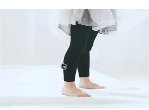 Vue détaillée de leggings pour bébés noirs côtelés avec un joli pompon moelleux à la cheville.