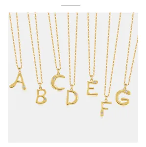 Nahaufnahme goldener Buchstaben-Halsketten mit zarten Ketten und funkelnden Steinakzenten.