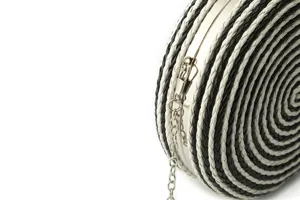 Detail shot of black and white woven round clutch bag showing texture and metal chain.