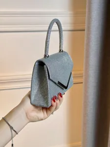 Détail de pochette de soirée argentée scintillante avec serrure V et poignée chic.