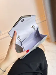 Détail de pochette de soirée argentée pailletée avec doublure et chaîne en métal.