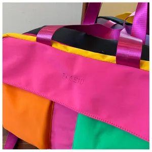 Close-up detail of color-block travel duffel bag, vibrant stitching and glossy purple straps.