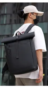 Close-up detail of the black waterproof roll-top backpack worn outdoors by a male model.