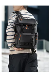 Detail view of a stylish black men's backpack with orange accents worn outdoors.