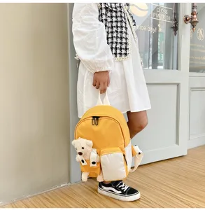 Dettaglio dello zaino con orsetto peluche, tela gialla e tasca frontale per bambini.