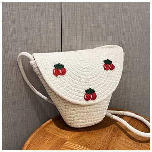 Primo piano della borsa a tracolla in paglia intrecciata beige con dettagli di ricamo ciliegie.