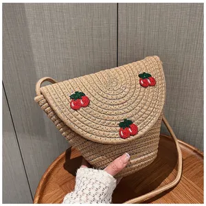 Primo piano di una borsa a tracolla in paglia con graziosi dettagli di ciliegie ricamate.