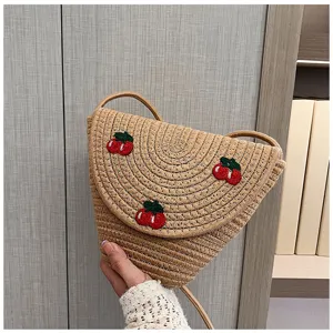Dettaglio di borsa a tracolla in paglia con ricamo di ciliegie rosse, perfetto stile estivo.