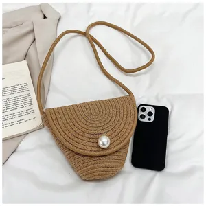 Dettaglio della borsa a tracolla estiva in paglia intrecciata con chiusura di perla e trama.