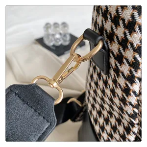 Detailopname van de damestas schouderband sluiting met klassiek houndstooth patroon en goud metaal.